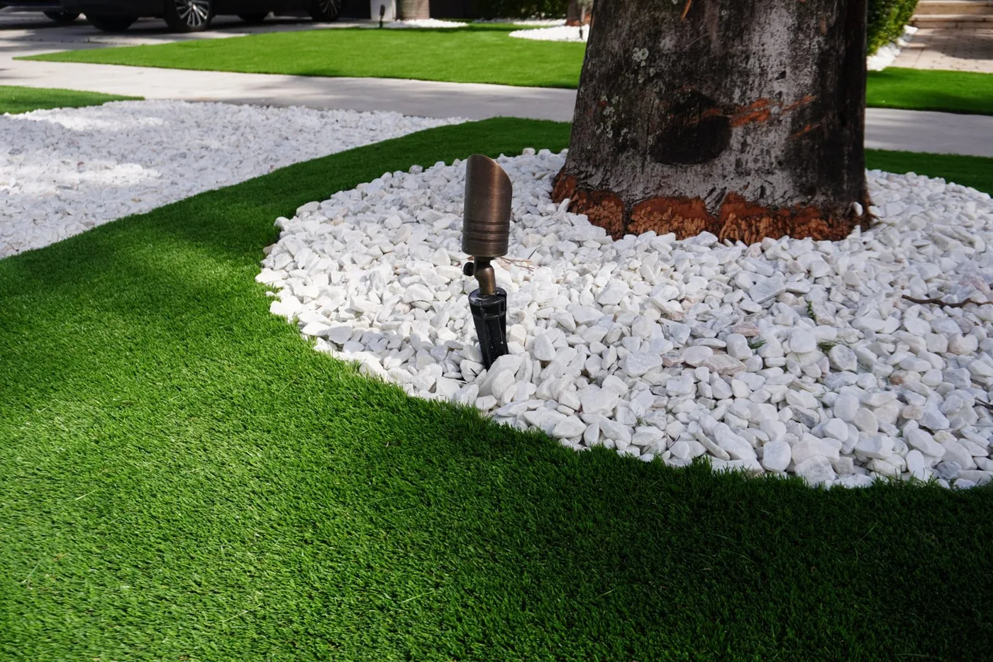 Artificial turf with a white rock ring and uplighting around a palm