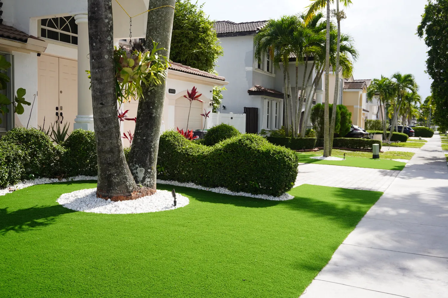Finished artificial turf front lawn with palms and rock tree rings by M&R Outdoor Living