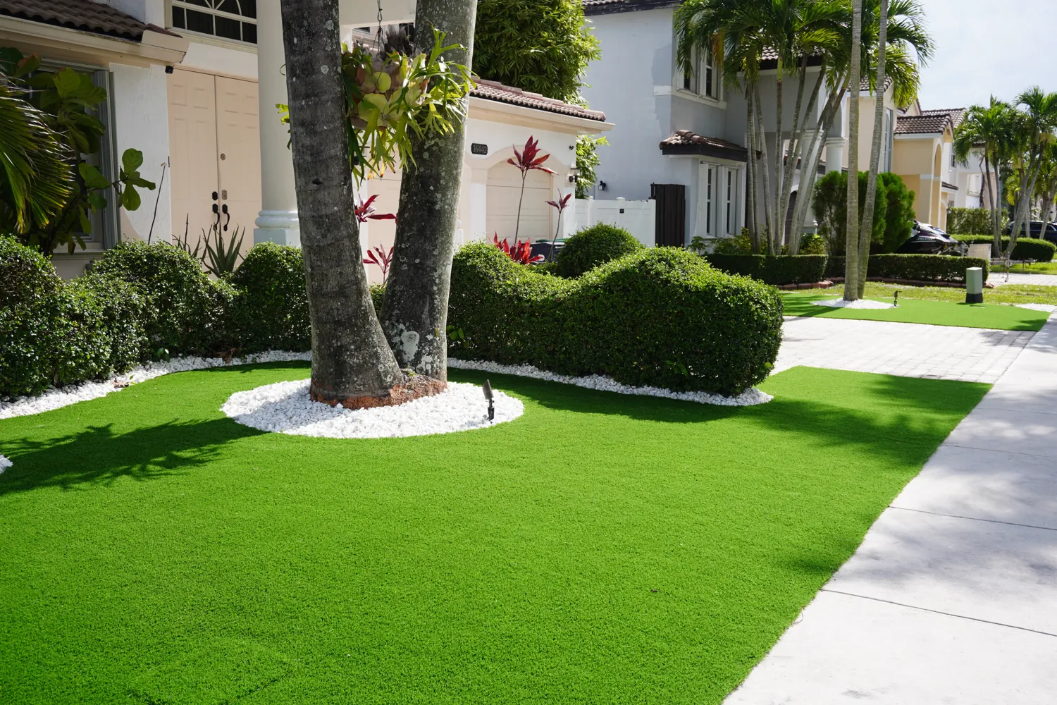 Artificial turf with white rock tree rings and manicured hedges in South Florida
